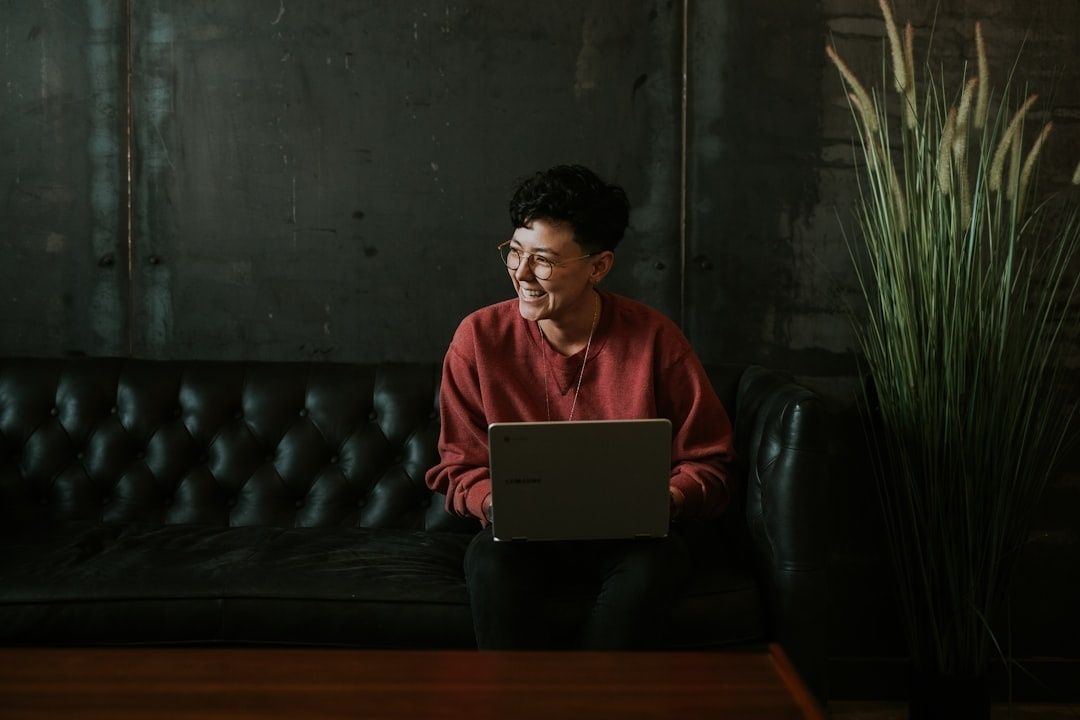 Leende person med laptop på en mörk soffa, fokuserad på sitt arbete