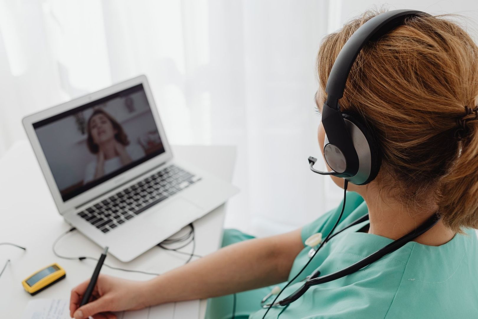 Kvinna med headset antecknar under ett videomöte på laptop