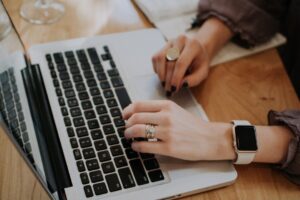 Person arbetar vid laptop med anteckningsbok och digital klocka