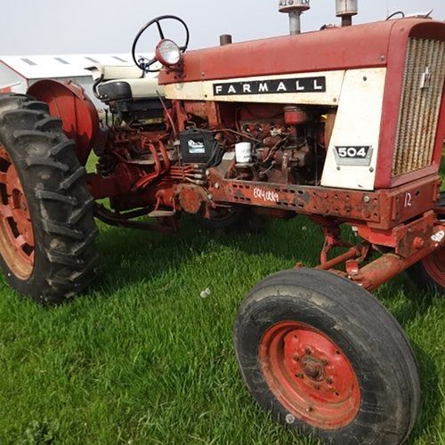 En röd vintage Farmall 504 traktor på en gräsmatta framför en lada.