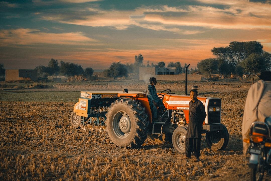 En röd traktor med maskintillbehör på ett fält i solnedgång.